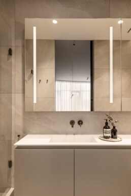 Ванна кімната з білою раковиною та дзеркалом з підсвічуванням / Bathroom with a white sink and backlit mirror